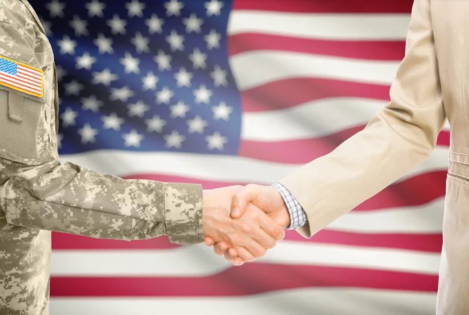 Image of a soldier and business man shaking hands with flag in background
