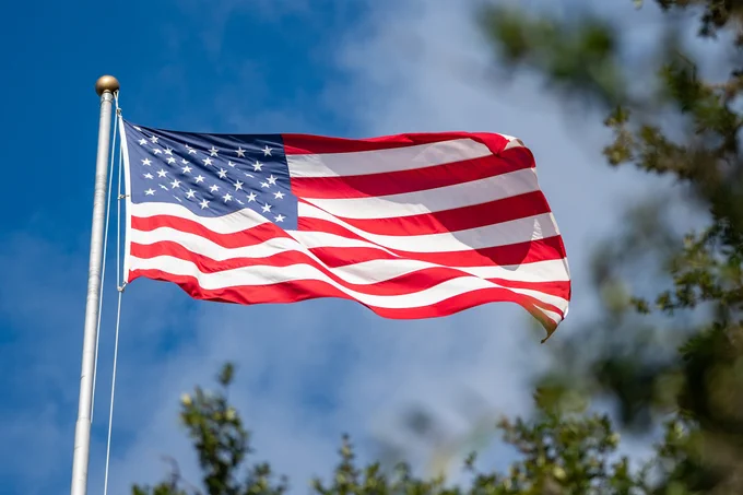 looking through leaves on an oak tree at an american flag waving on campus