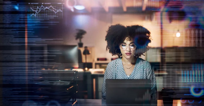 A young female programmer using a laptop while working late in her office.