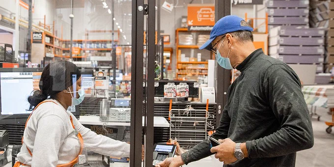 A customer makes a purchase from a Home Depot associate  while both wear masks.