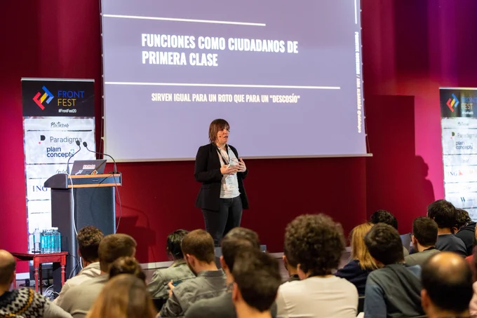 Estoy sobre el escenario dando la charla, se ve a la audiencia atendiendo y de fondo una slide explicando las funciones de javascript como ciudadanos de primera clase
