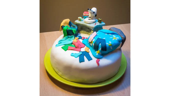 A fruitcake decorated with fondant icing to look like a messy bedroom with clothes on the floor, with a microscope set up on the desk for working from home.
