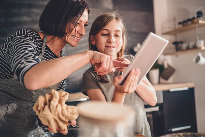 Mother and daughter baking and using tablet