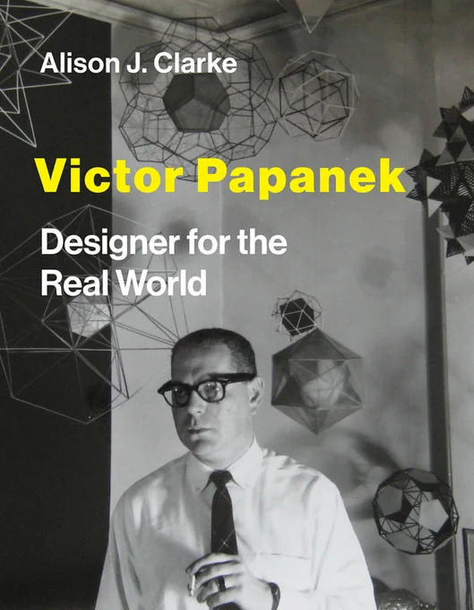 Book cover of the new monograph, Victor Papanek: Designer for the Real World, by Alison J. Clarke and forthcoming in March 2021 by MIT Press. The cover is a black and white period photograph of Victor Papanek dressed in a shirt and tie, with characteristic eyeglasses and lit cigarette, surrounded by various sizes of tetrahedra models hanging from the ceiling and walls. 