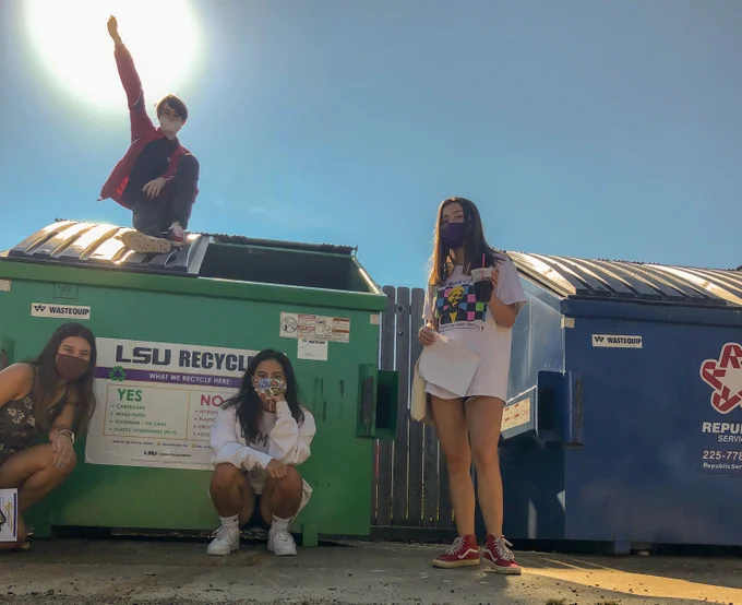 a group of students in masks pose in front of and on top of a recycle bin