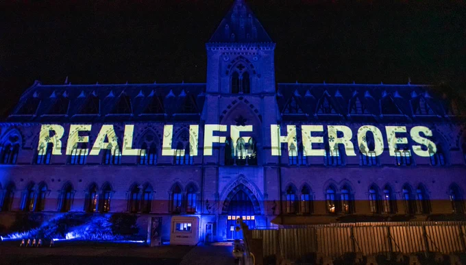 Illuminated message on the facade of the Oxford Museum of Natural History saying Real life heroes in cream letters on blue background