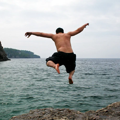 A person jumping off a cliff into an ocean, arms spread out wide.