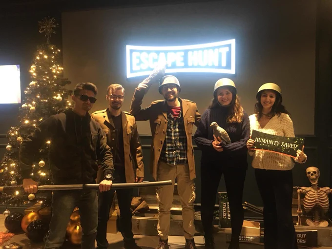 some of the kalli lab posing outside an escape room sign holding all sorts of props