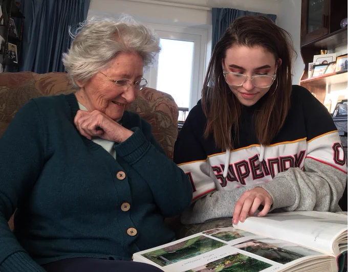 Mum and her granddaughter smiling and looking at a photo album together
