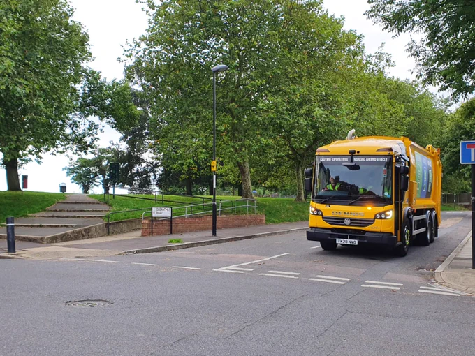 Image shows a recycling vehicle in a countryside street surrounded by trees and greenery.