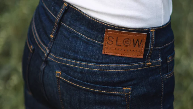 A closeup of a person seen from behind, wearing a white-tshirt and Slow Hemp blue jeans. Just the lower part of the shirt and the back part of the jeans with the tag is visible.