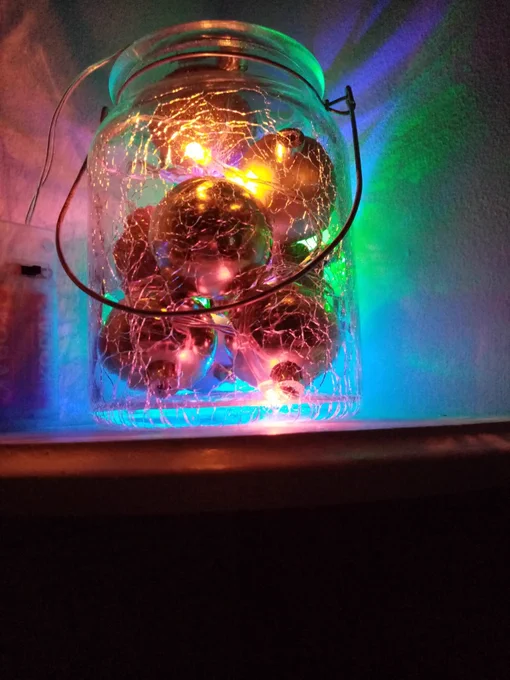 A Christmas decoration - a jar with glowing gold baubles in.
