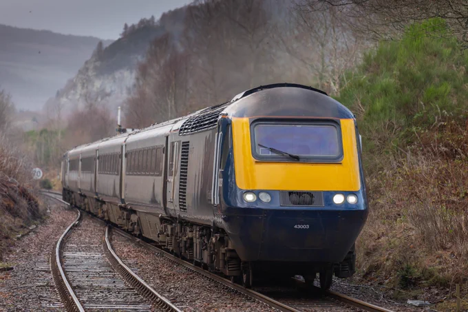 A high-speed train approaches the camera against a wintry backdrop of bare trees and overcast skies.