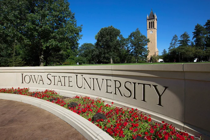 Summertime view of the campanile behind the engraved Iowa State University wall.