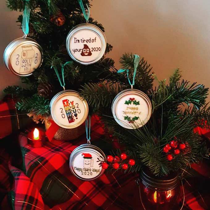 A small christmas tree and a pine branch in a red mason jar sit on a red and green plain cloth. They are decorated with Put a Lid on 2020 Ornaments, including 2 Braille ornaments, the School Time "Thank You!" Ornament, "ROLL WITH IT! 2020" Toilet Paper ornament, and "I'm tired of your (poop emoji), 2020" ornament.