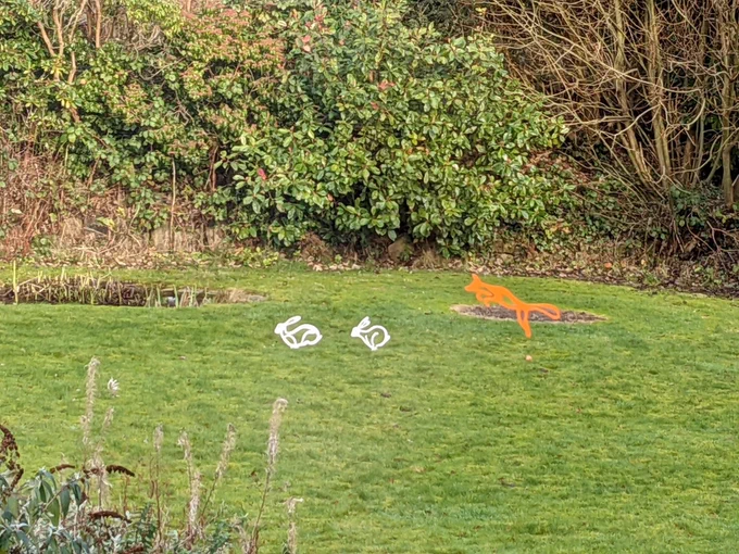 Thin animal sculptures : orange fox pouncing toward  two white hares running