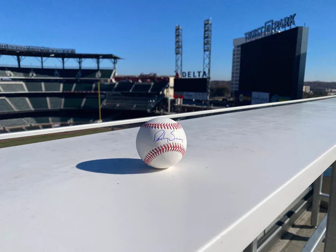 A baseball autographed by Dansby Swanson with Truist Park in the background.