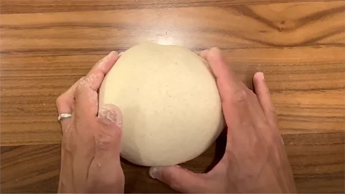 overhead view of hands holding round bread dough on a wood table surface