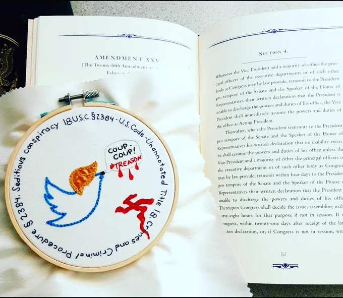 An embroidery hoop with fabric sits on a small book open the Amendment 25, section 4 of the U.S. Constitution. The piece is white silk fabric with the outline of the blue Twitter bird in the center. The bird has blond hair approximating the style of donald trump and a black Hitler mustache. A word bubble is coming from the bird's mouth with "COUP-COUP!" in black and "#TREASON" in red. Blood drips from the word bubble into a swastika shaped puddle on the floor. The words "18 U.S.C. section 2384 - U.S. Code - Unannotated Title 18. Crimes and Criminal Procedure section 2384. Seditious conspiracy" encircle the above image in dark blue thread.