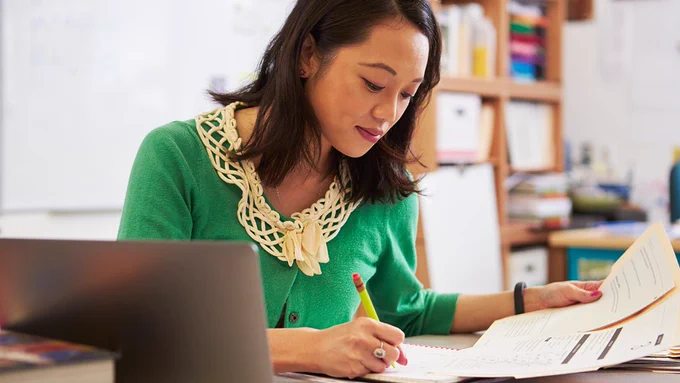 Teacher sitting at a desk marking a paper.
