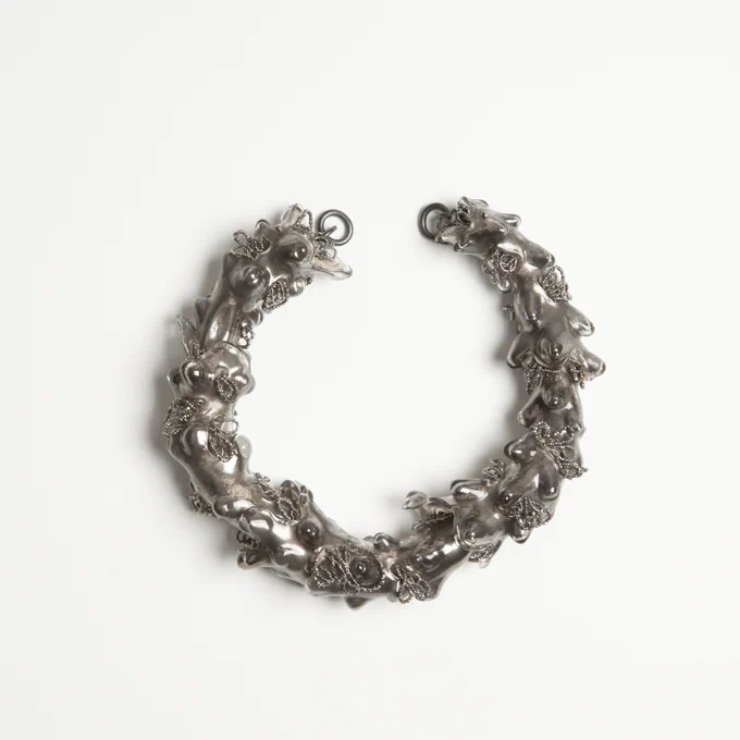 A necklace composed on interlocking sections of smoothly polished irregular shaped glass pieces tinted silver. Chains of silver beads make loops between the interlocking glass forms