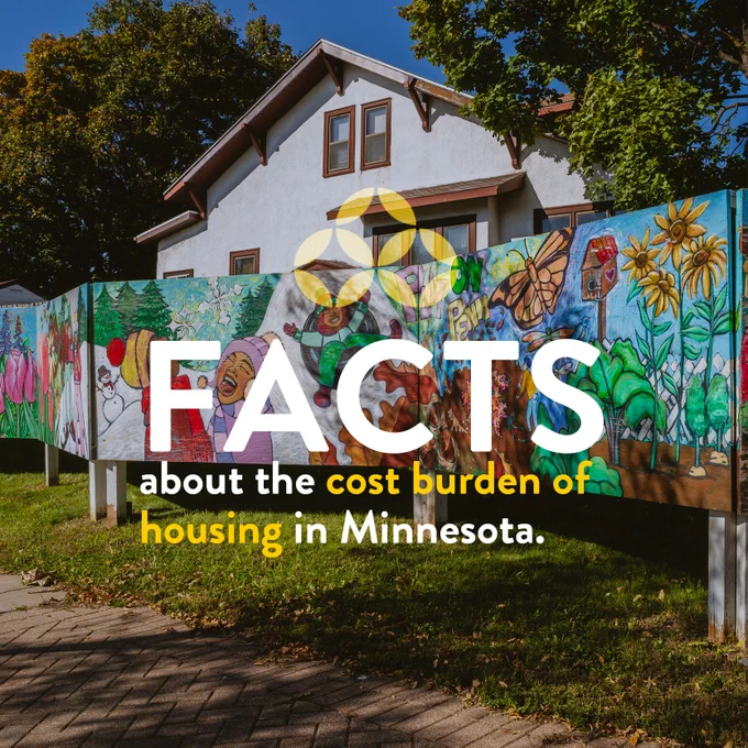 A fence painted with a bright colored mural depicting Minnesota seasons in front of a two-story white stucco house with brown trim. 