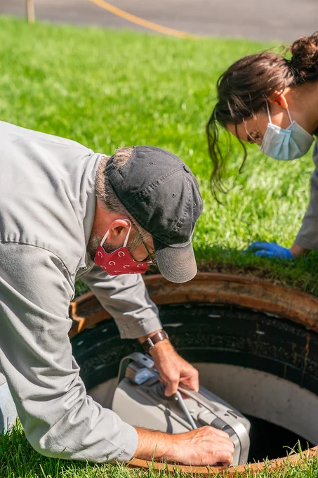 Geoffrey Holm, Associate Professor of Biology along with Michelle Landstrom, Surveillance and Monitoring Technician, use a GLS Sampler to collect samples of waste water for detection of COVID-19 around the Colgate University campus.