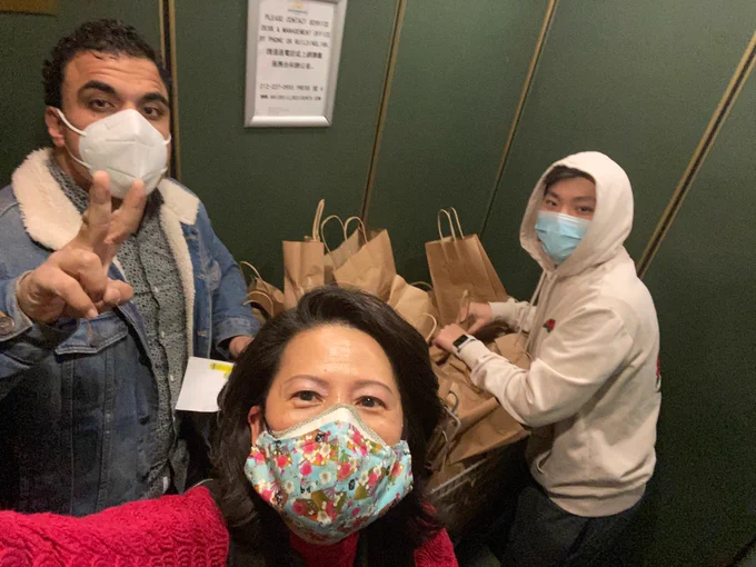 Jenny and crew in an elevator with a cart full of meals in brown paper bags