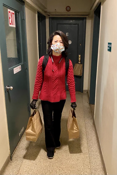Jenny in red sweater hold two bags of meals in a residential hallway, one bag of food left on door behind her