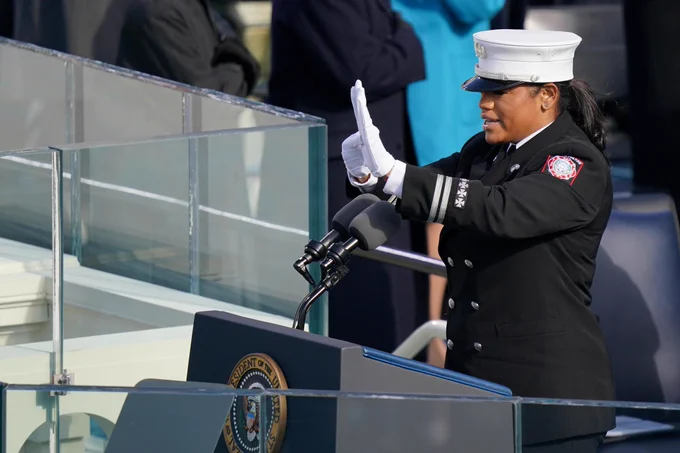 Andrea Hall a black fire captain stands in front of a podium with a Presidential seal and sings
