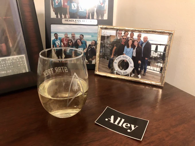 Stemless glass of champagne on a shiny wooden table with framed photos of friends on the table behind the glass