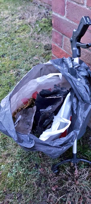 Photo shows open black bin bag. You can see various other plastic bags inside it. Leaning against the bag is a litter picker.