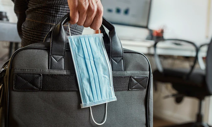 Person holding a laptop bag, facemask in hand.