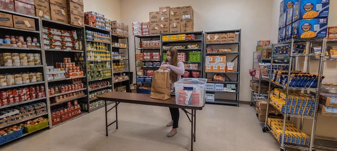A student stands in the center of Amarillo College's food pantry, loading a bag of groceries. During the pandemic, Amarillo College kept its food pantry stocked and open, but moved the order form online.