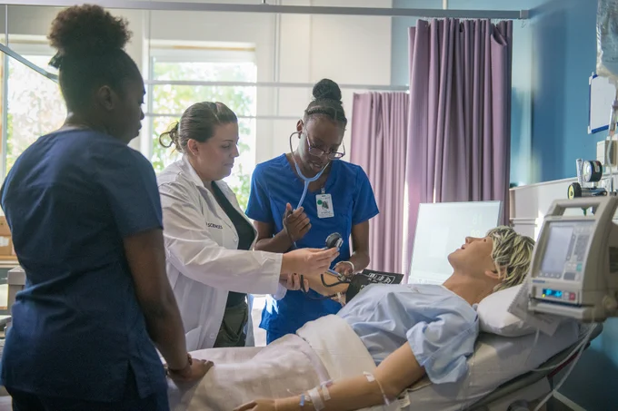 A female faculty member helps two female nursing students with a simulated patient in our nursing simulation lab. 