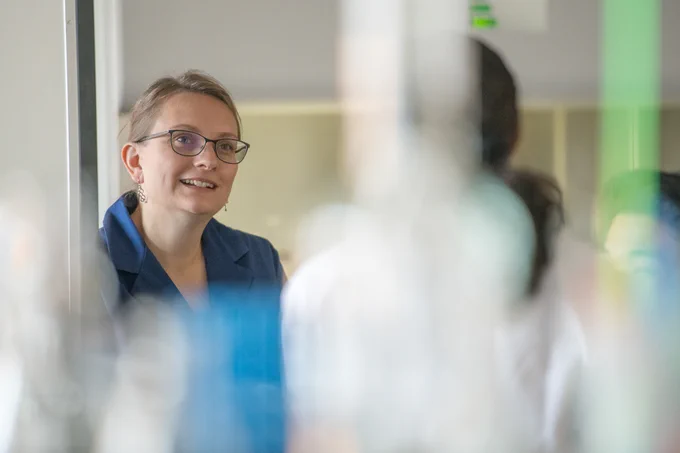 Dr. Denina Simmons speaks with a student in the lab. The view of the student is obstructed by beakers and other lab items. 