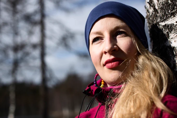 Nainen nojaa puuhun ja katsoo horisonttiin. Aurinko paistaa. 