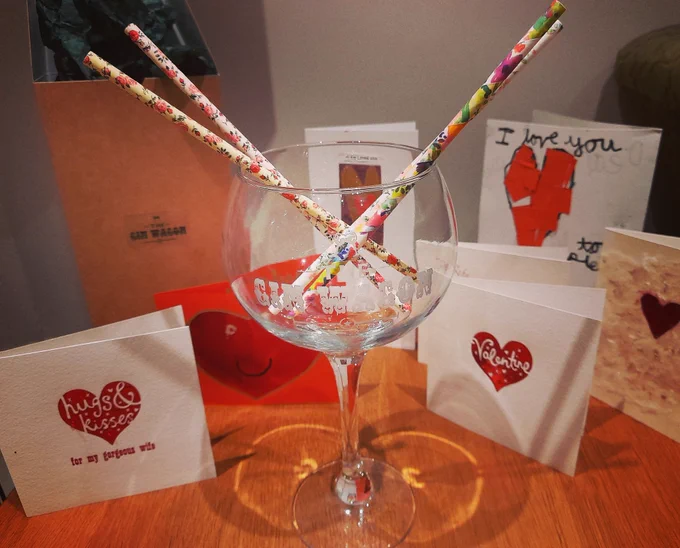 Gin glass containing paper straws, in front of Valentine's cards