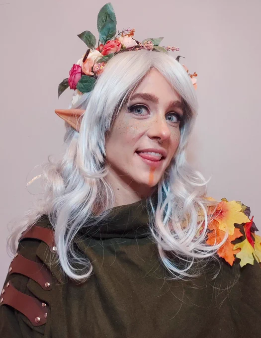 Photo of me dressed as Oldiel, my OC. I'm wearing a long white wavy wig, long pointed ears, a flower crow and a dark green top with autumn leaves over one shoulder.