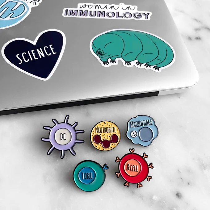 Photo of immune cell enamel pins and some science themed stickers.
