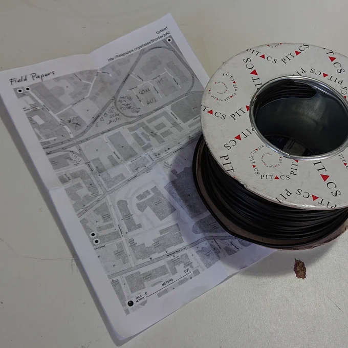 A printed out map annotated with hand-written labels, next to a 100m reel of wire