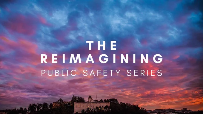 University of San Francisco logo at the top left corner. In the middle, large white text reading, “the reimagining public safety series” on a blue, purple, and pink cloudy sunset background.