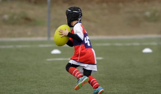 Child in rugby gear running on a field with a rugby ball