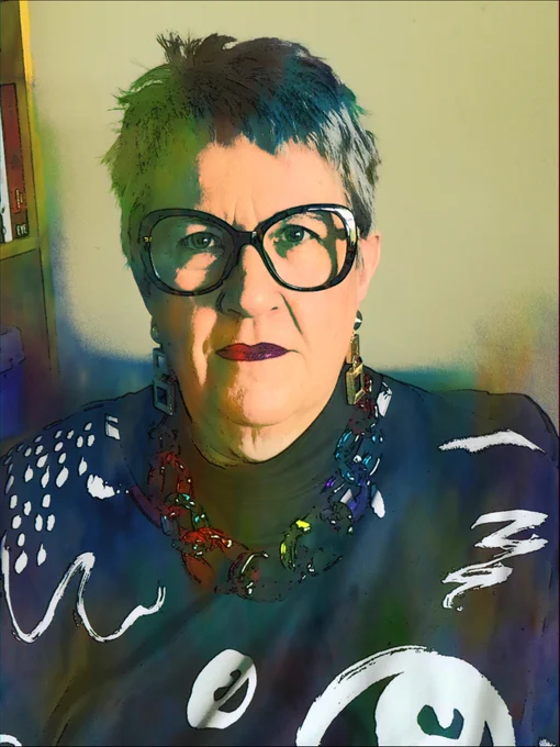 Digitised image of the mighty Vici Wreford-Sinnott in a black and white patterned jumper, big multicolour necklase, bright dark red lips, big black glasses, and short blue hair, looking directly and determinedly at the camera.