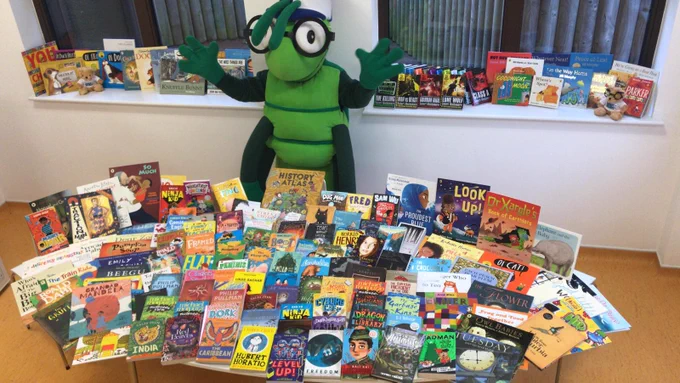KM Charity Team mascot Buster Bug with the bumper book donation from Scholastic UK.