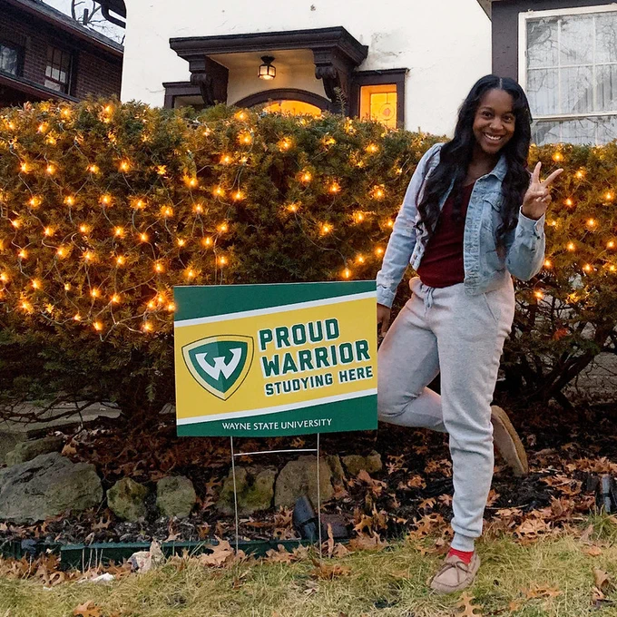 Woman holding up a peace sign next to a sign in the ground