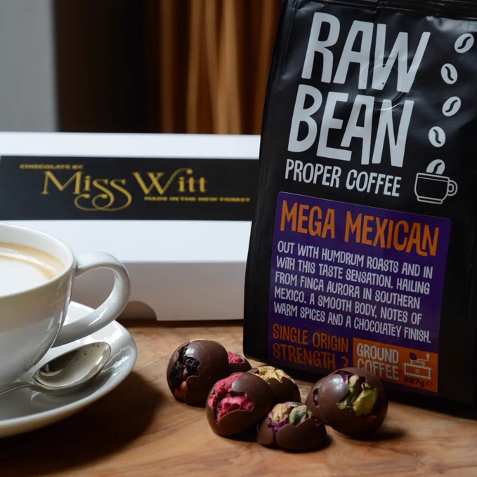 Raw bean Finca Aurora Mega Mexican filter coffee on a wooden board with beautifully present Miss Witt chocolates and a cup and saucer with silver spoon. Truffles flavored Raspberry, pistachio, fruit & nut and fudge