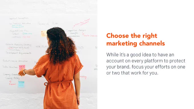 A woman with long curly hair, wearing an orange dress, stands in front of a whiteboard with brainstorm ideas and post-it notes on it.