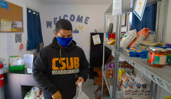 Student wearing face mask and CSUB sweater walking through the campus food pantry holding a bag. 
