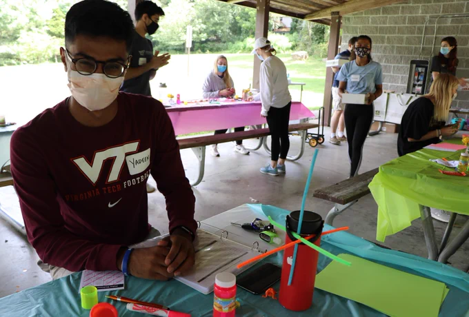 A Hokie Wellness peer educator smiles behind his mask as he sits at a table doing craft activities during a Hokie Wellness training retreat.